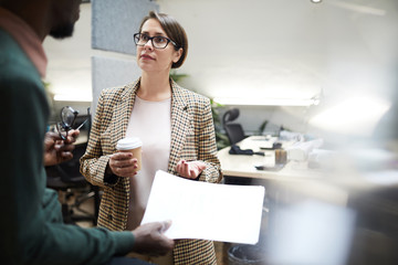 Waist up portrait of female business manager talking to African-American colleague during coffee break in office, copy space