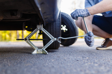 Mechanic in gloves lifts the car Jack on the side of the highway. Man is preparing to change the flat wheel lifting the car with a Jack on the side of the highway.