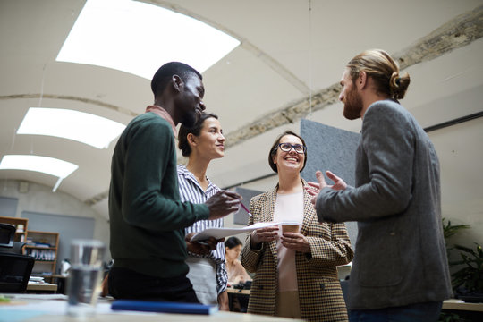 Low Angle View At Multi -ethnic Group Of Business People Laughing Happily While Chatting During Coffee Break In Office, Copy Space