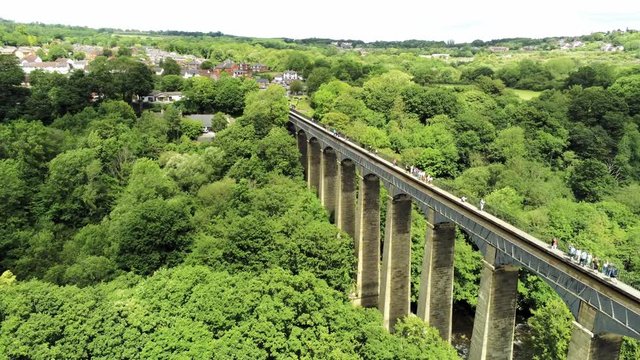 Pontcysyllte Aqueduct arch bridge canal waterway crossing. Fast aerial across sunny green countryside & structure.
