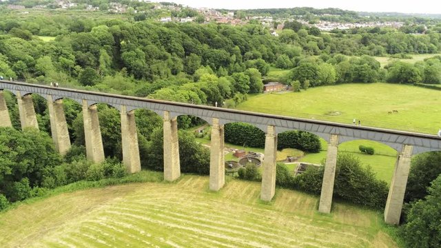 Pontcysyllte Aqueduct arch bridge canal waterway crossing. Descending tilt up reveal across rural Welsh countryside.