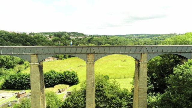 Pontcysyllte Aqueduct arch bridge canal waterway crossing. Horizontal pull back aerial as people cross.