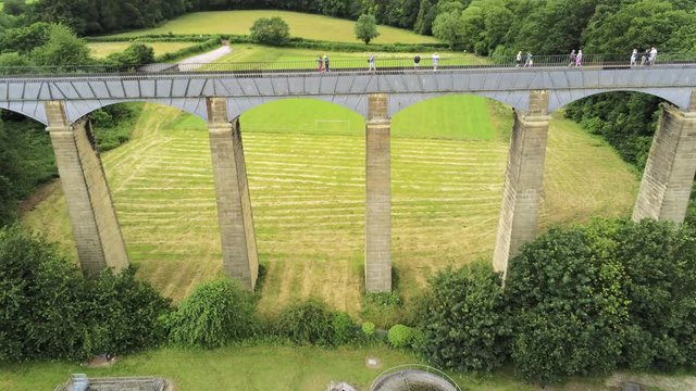 Pontcysyllte Aqueduct arch bridge canal waterway crossing. Descending aerial towards arch as people walk across.