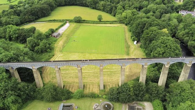 Pontcysyllte Aqueduct arch bridge canal waterway crossing. Descending aerial as people walk across landmark.