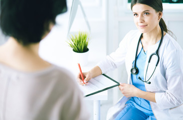 Doctor and patient discussing medical problems in a hospital consulting room. Doc filling in a...