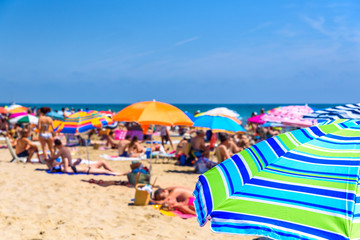 Colorful beach umbrella stuck in the sand surrounded by a group of bathers in summer, near the Mediterranean sea.