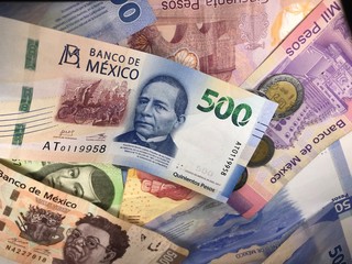 Many mixed Mexican peso bills spread over a wooden desk