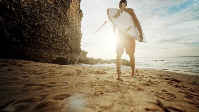 Guy walking on the beach in the morning. Big waves crash and break. Silhouette of female surfer with surfboard in his hand on beautiful golden evening. slow motion footage