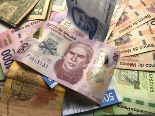 Many mixed Mexican peso bills spread over a wooden desk