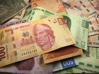 Fototapeta na wymiar Many mixed Mexican peso bills spread over a wooden desk