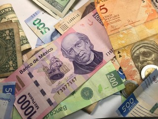 Many mixed Mexican peso bills spread over a wooden desk