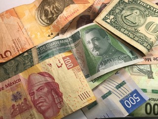 Many mixed Mexican peso bills spread over a wooden desk