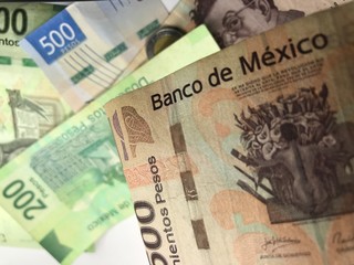 Many mixed Mexican peso bills spread over a wooden desk