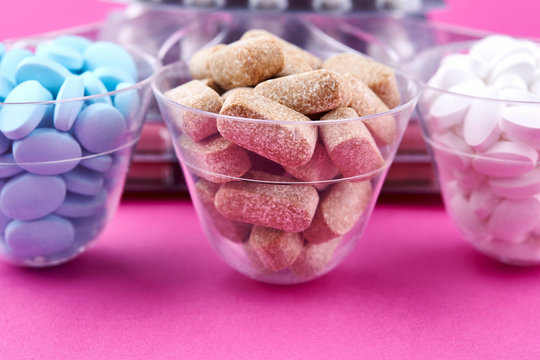 Blue brown and white pills in graduated glass on pink background
