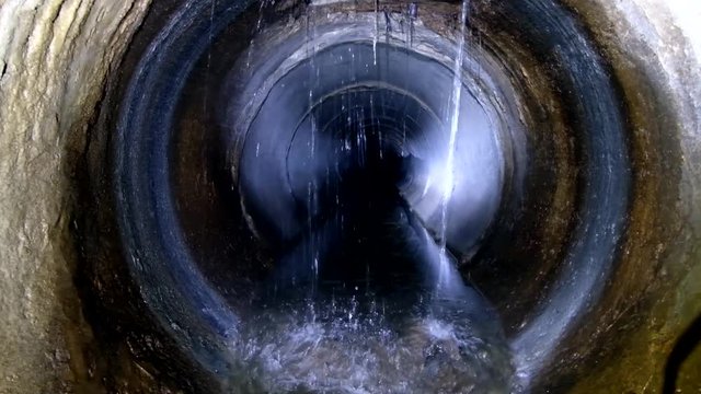 Dark underground sewer round concrete tunnel. Industrial wastewater and urban sewage flowing throw sewer pipe