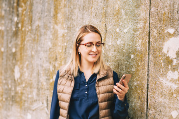 Young businesswoman using phone outside, reading or texting message, wearing glasses and blue dress