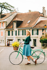 Retro styled portrait of beautiful young woman, wearing vintage clothes, holding mint color bicycle with yellow flowers placed in basket