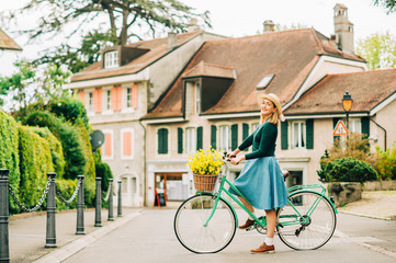 Fototapeta na wymiar Retro styled portrait of beautiful young woman, wearing vintage clothes, holding mint color bicycle with yellow flowers placed in basket