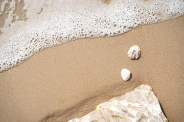 Fototapeta na wymiar sea wave with bubbles on the sand beach And rocks with white shells