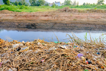 Garbage waste is dumped along the canal. The waste water is dirty with black.