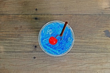 Refreshing blue hawaii italian soda with cherry on top on wooden table, top view.