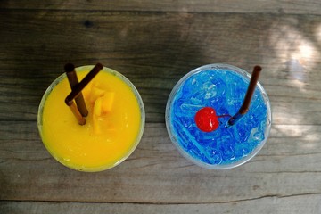 Refreshing Mango smoothie and blue hawaii italian soda with cherry on top  on wooden table, top view.