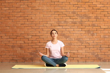 Beautiful woman practicing yoga near brick wall