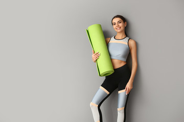 Sporty woman with yoga mat on grey background