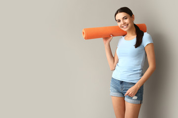 Beautiful woman with yoga mat on grey background