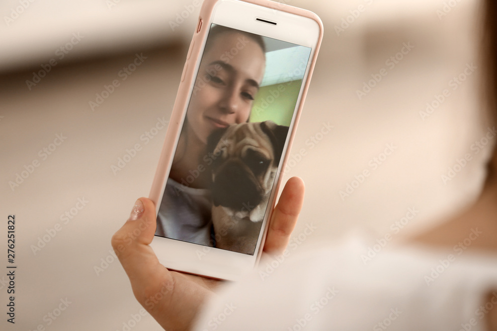 Poster Teenage girl taking selfie with cute pug dog at home, closeup