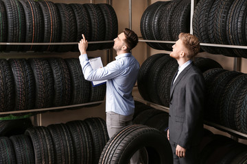 Seller helping man to choose tires in car store