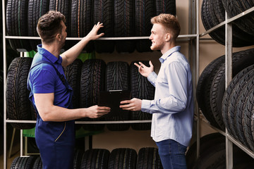 Seller helping man to choose tires in car store