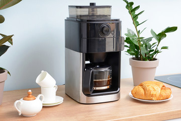 Modern coffee machine, cups and croissants on kitchen table