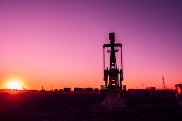 Oil pumps are running in the sunset at the oil field.