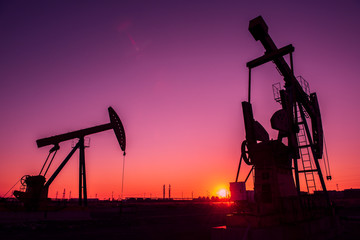 Oil pumps are running in the sunset at the oil field.