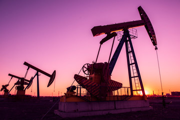 Oil pumps are running in the sunset at the oil field. - obrazy, fototapety, plakaty