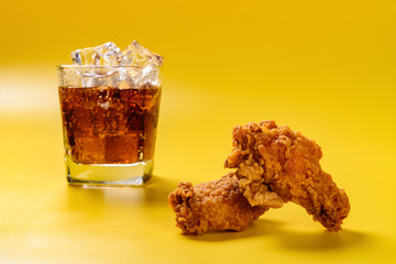 side view fresh deep fried chicken drumstick and wing with cup of iced cola on yellow background