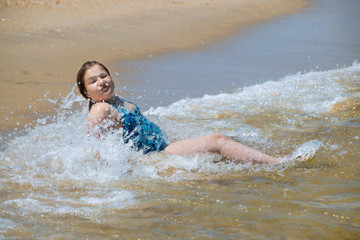 Cute little girl in beautiful with water and sand sitting at s shore of the sea on empty peaceful beach