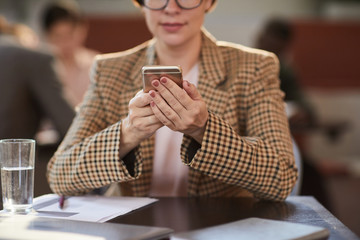 Cropped portrait of contemporary businesswoman holding smartphone while working at table in cafe, copy space