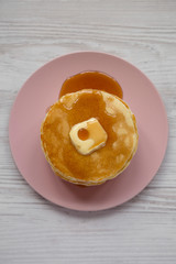 Stack of homemade pancakes with butter and maple syrup on a pink plate, top view. Overhead, from above, flat lay.