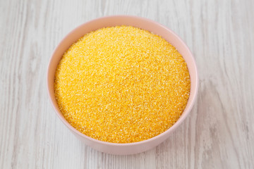 Dry organic Masarepa corn meal in a pink bowl over white wooden background, low angle view. Close-up.