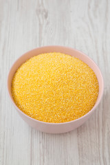 Dry organic Masarepa corn meal in a pink bowl over white wooden background, low angle view. Closeup.