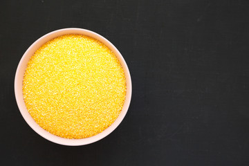 Dry organic Masarepa corn meal in a pink bowl over black surface, top view. Flat lay, overhead, from above. Copy space.