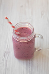 Glass jar with smoothie made of banana, black currant, coconut milk on a white wooden table, side view. Close-up.