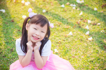 Little asian girl sitting and smiles on grass field in park
