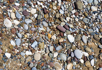 Multi-colored large sea pebbles of various shapes on the sandy shore of the Mediterranean sea for background