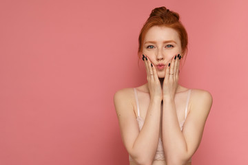 Young redhead woman wearing lace bra makes a kissy face posing over pink background