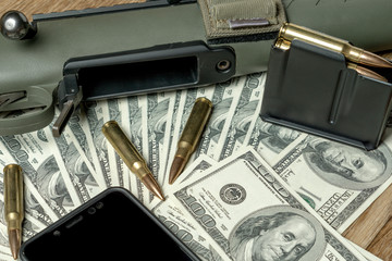 Rifle, magazine and cartridges on money. Concept for crime, contract killing, paid assassin, terrorism, war, global arms trade, weapons sale. Illegal hunting, poaching. Black screen smartphone