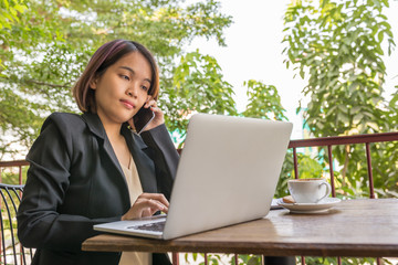 Woman using cellphone and laptop next to cup of coffee