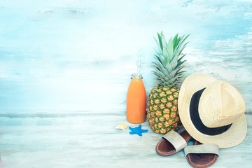 Summer concept stillife - ripe pineapple, straw hat, flip-flops and a bottle of multivitamin juice...